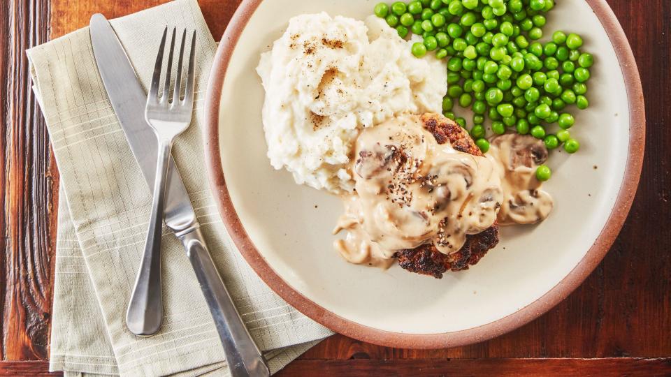 easy weeknight salisbury steak with gravy and mashed potatoes and peas on two plates with silverware