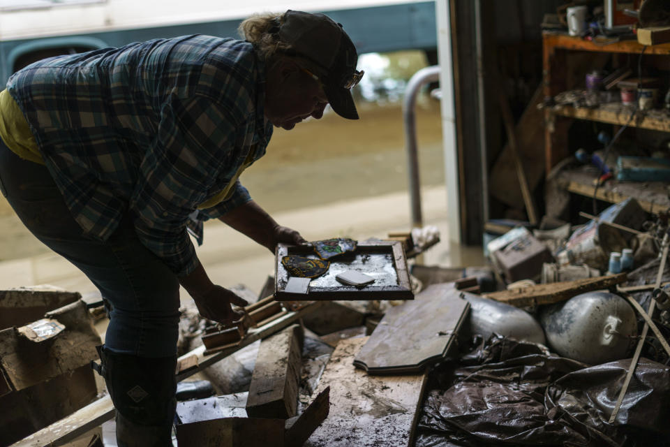 Lindi O'Brien picks up a commendation plaque to her father's police service from the barn of her parent's home badly damaged by the severe flooding in Fromberg, Mont., Friday, June 17, 2022. (AP Photo/David Goldman)