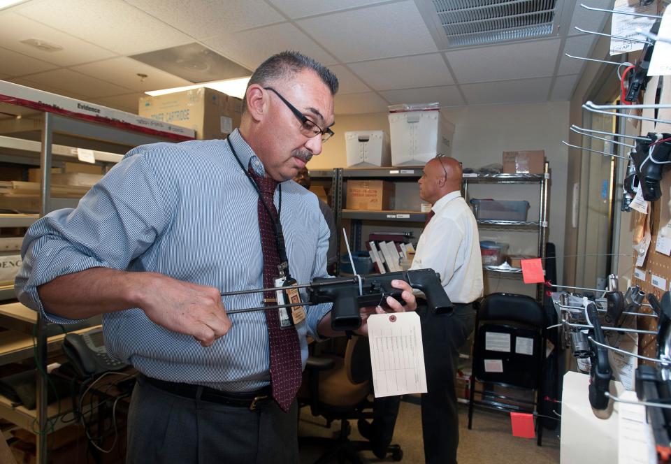 Asst. State Attorney John Molchan, left, looks over some of the weapons recovered by local law enforcement officers and held in the evidence locker at the local Alcohol Tobacco Firearms and Explosives, field office.