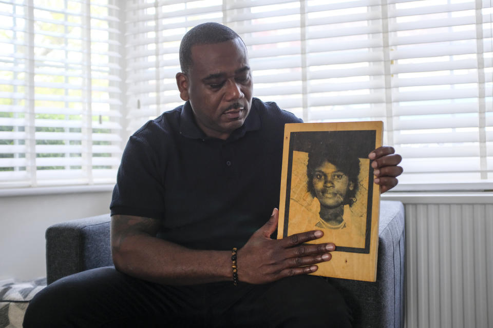 Lee Lawrence poses with a picture of his mother, Cherry Groce, in London, Wednesday, April 21, 2021. Lawrence's mother, Cherry Groce, was shot by police during a raid on her London home in 1985. She was left paralyzed from the waist down and died in 2011 after spending 26 years in a wheelchair. Her shooting triggered the 1985 Brixton riots, and her family have been fighting for justice ever since. (AP Photo/Alberto Pezzali)