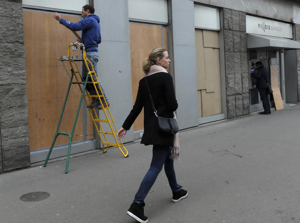 A woman walks past a worker fixing wooden pieces on a bank window near the Champs-Elysees avenue, Friday, Dec. 7, 2018 in Paris. Drastic security measures will put a lockdown on downtown Paris on Saturday as French authorities try to prevent another outbreak of violence during anti-government protests. (AP Photo/Bertrand Combaldieu)