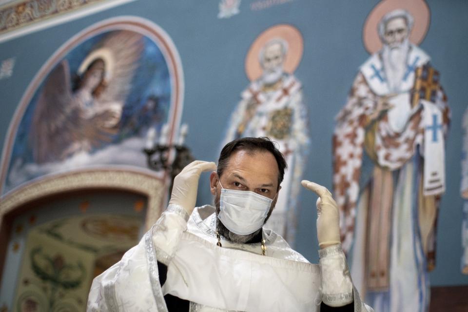 In this photo taken on Tuesday, June 2, 2020, Father Vasily Gelevan, wearing a face mask and gloves to protect against the coronavirus, prepares to conduct a service at the Church of the Annunciation of the Holy Virgin in Sokolniki in Moscow, Russia. In addition to his regular duties as a Russian Orthodox priest, Father Vasily visits people infected with COVID-19 at their homes and hospitals. (AP Photo/Alexander Zemlianichenko)