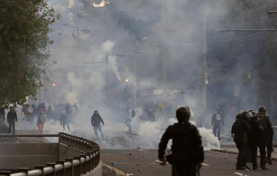 Protesters stand in clouds of tear gas launched by police to disperse them, in Quito, Ecuador, Friday, Oct. 4, 2019, during a nationwide transport strike that shut down taxi, bus and other services in response to a sudden rise in fuel prices. Ecuador's President Lenín Moreno, who earlier declared a state of emergency over the strike, vowed Friday that he wouldn't back down on the decision to end costly fuel subsidies, which doubled the price of diesel overnight and sharply raised gasoline prices. (AP Photo/Dolores Ochoa)