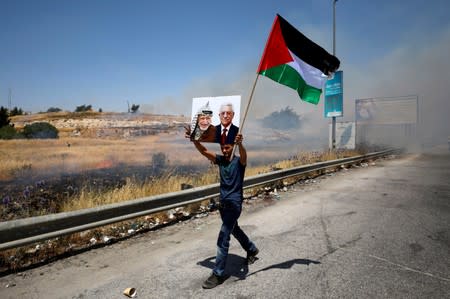 Demonstrator holds a Palestinian flag and a picture of late Palestinian leader Arafat and President Abbas during a protest in the Israeli-occupied West Bank