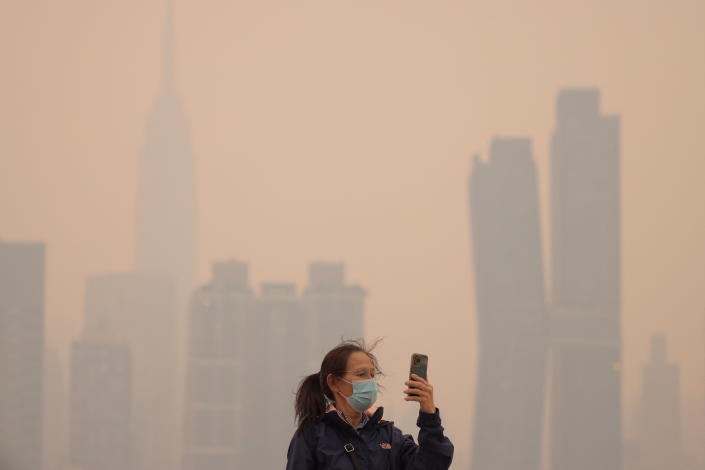 A person wearing a mask uses a cellphone as haze and smoke from Canada's wildfires hang over the Manhattan skyline on Wednesday.  (Andrew Kelly/Reuters)