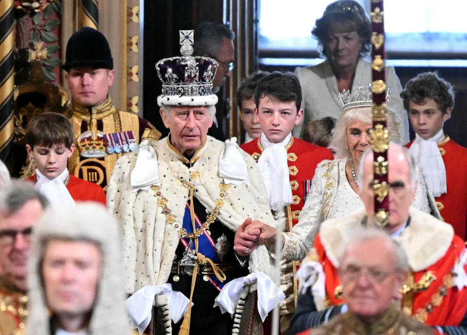 König Charles III. trägt eine Robe und eine Krone, neben ihm Königin Camilla 