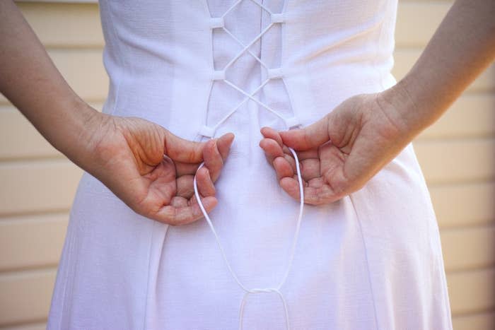 Back view of a person tightening the laces on a corset-style dress. No visible faces or identifying features