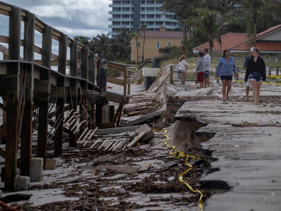 people walk down damaged beach boardwalk after hurricane nicole