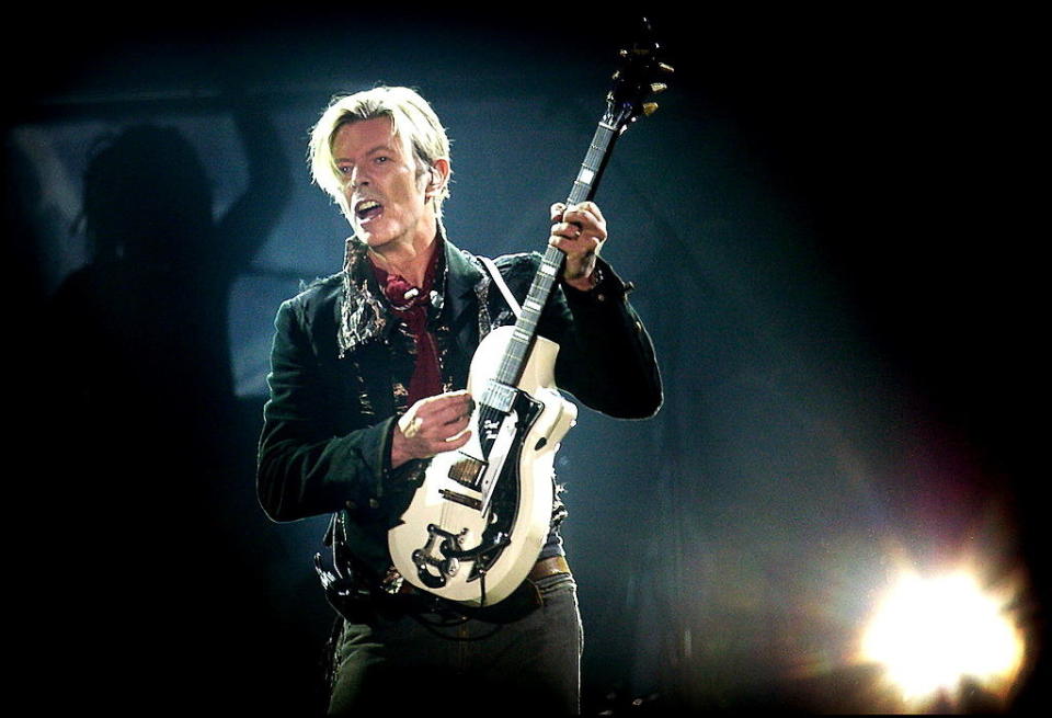 David Bowie holds us guitar upright as he plays it onstage