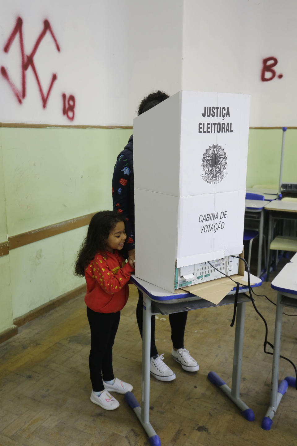 A woman, accompanied by a child, casts her vote in the general election in Sao Paulo, Brazil, Sunday, Oct. 7, 2018. Brazilians have started trickling to voting booths to choose leaders in an election marked by intense anger at the ruling class following years of political and economic turmoil. (AP Photo/Nelson Antoine)