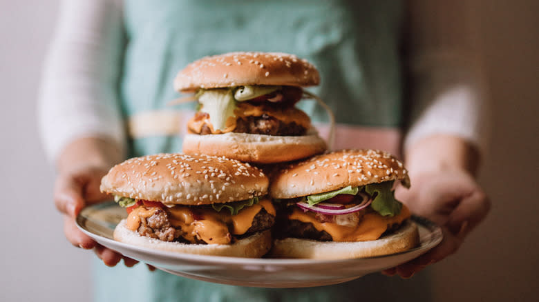 Hands holding platter of burgers