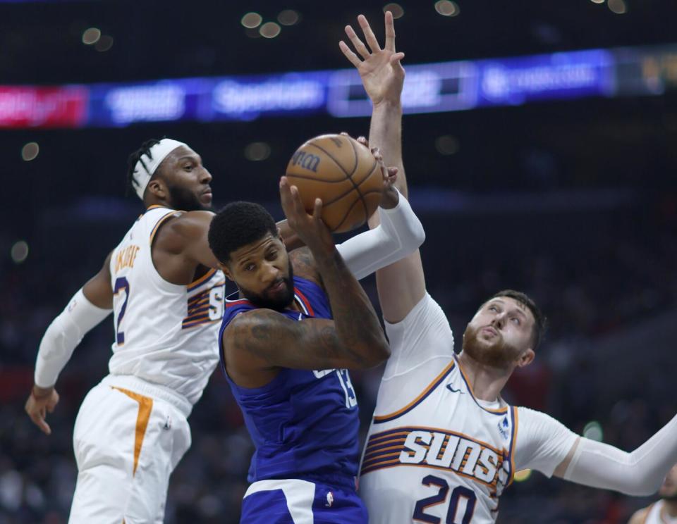 Clippers forward Paul George, center, grabs a rebound between Phoenix's Josh Okogie, left, and Jusuf Nurkic.