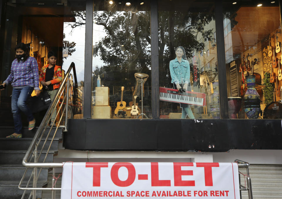 Una mujer y su hijo salen de una tienda de música mientras que en el local de abajo se ve un cartel de alquiler. La recuperación está siendo más costosa en Bangalore porque la pandemia ha golpeado duramente. (AP Photo/Aijaz Rahi)