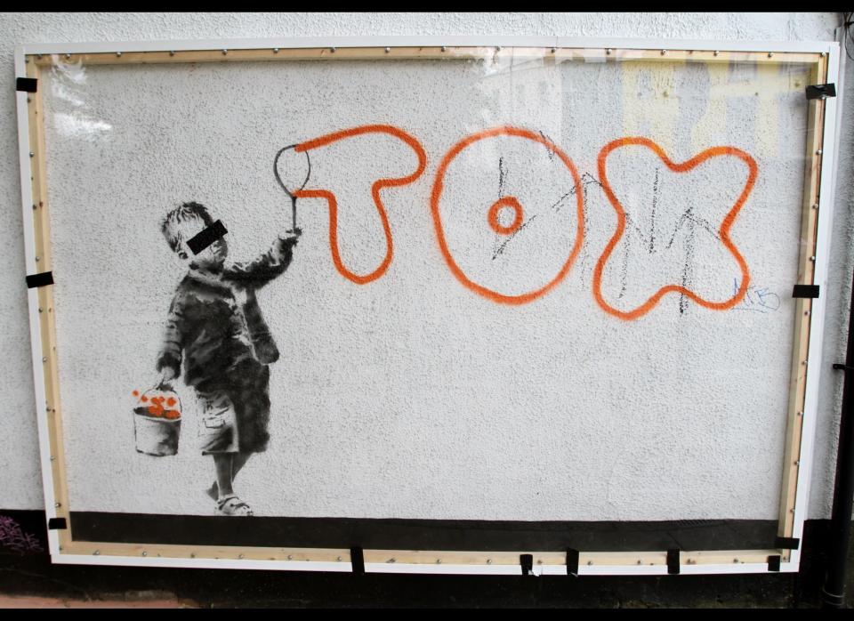 LONDON, ENGLAND - JUNE 24:  Passers by have a look at the new Banksy graffitti artwork in Camden Town on June 24, 2011 in London, England. The piece references the notorious London graffiti artist and tagger Tox who was recently found guilty of criminal damage and convicted.  (Photo by Stewart Stanley/Getty Images)