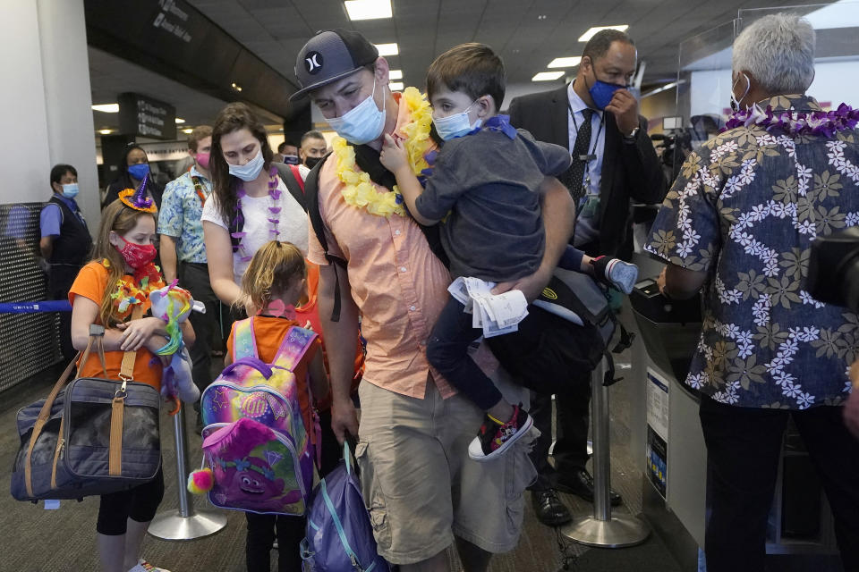 Hawaii residents Ryan Sidlow, center, carries his son Maxwell as their family boards a United Airlines flight to Hawaii at San Francisco International Airport in San Francisco, Thursday, Oct. 15, 2020. Coronavirus weary residents and struggling business owners in Hawaii will be watching closely as tourists begin to return to the islands on Thursday without having to self-quarantine upon arrival. (AP Photo/Jeff Chiu)