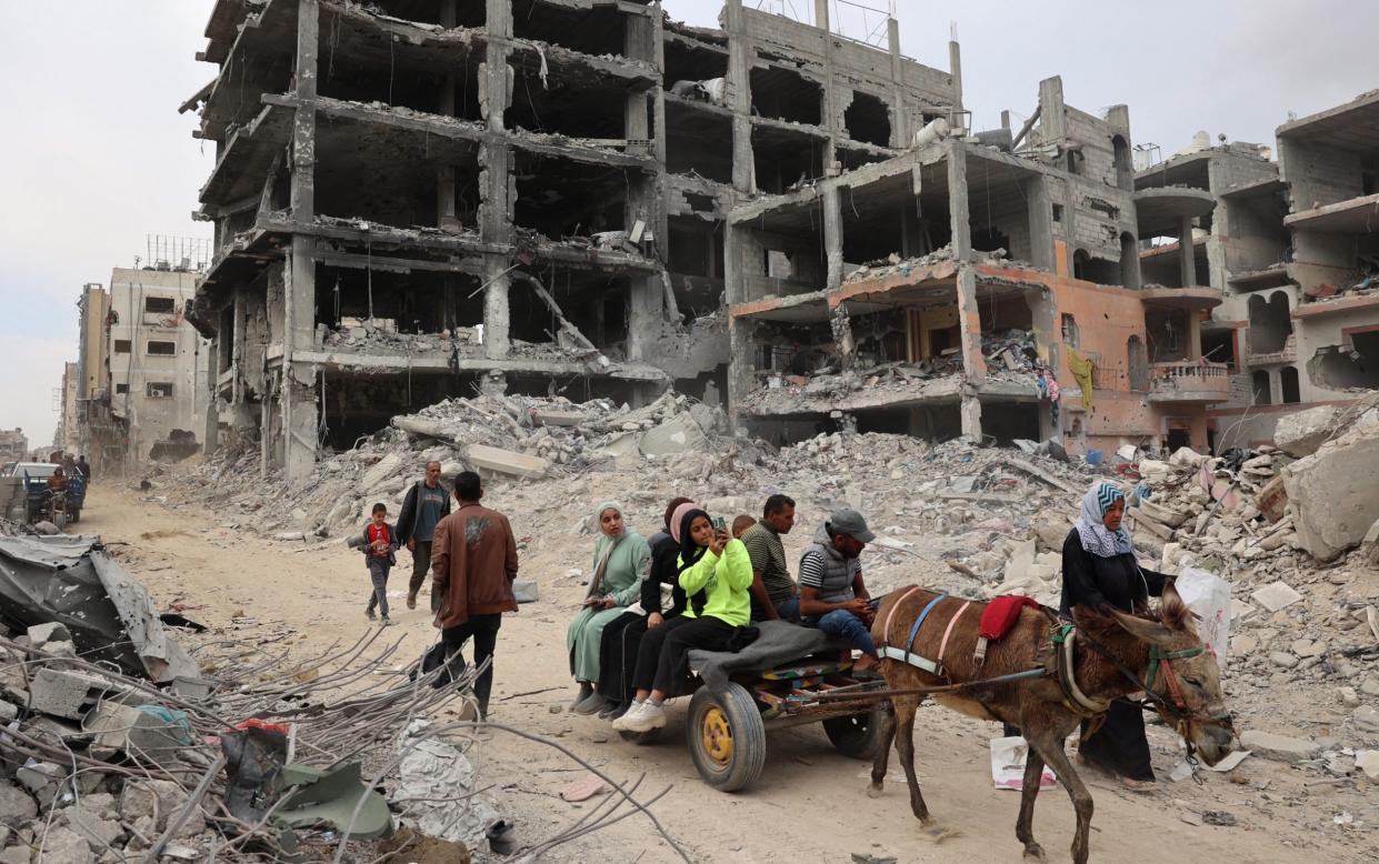 A Palestinian family riding on a carriage drawn by a donkey in front of a series of bombed-out buildings