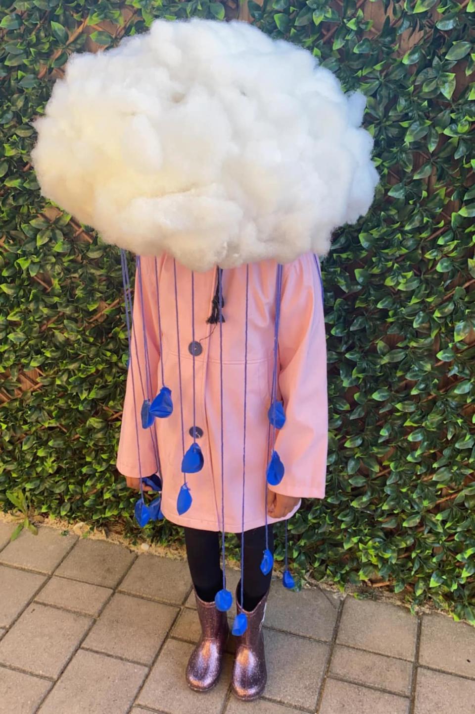 A girl dressed as a rain cloud with pillow fluff cloud hat, rain coat, gum boots and balloon string rain drops