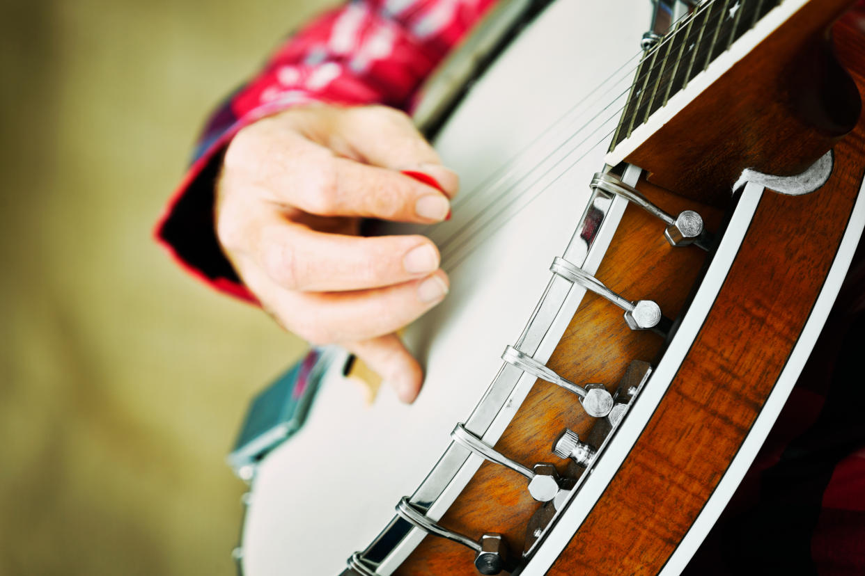 Cropped shot of a banjo being played with a pick (or plectrum) by a feminine hand.