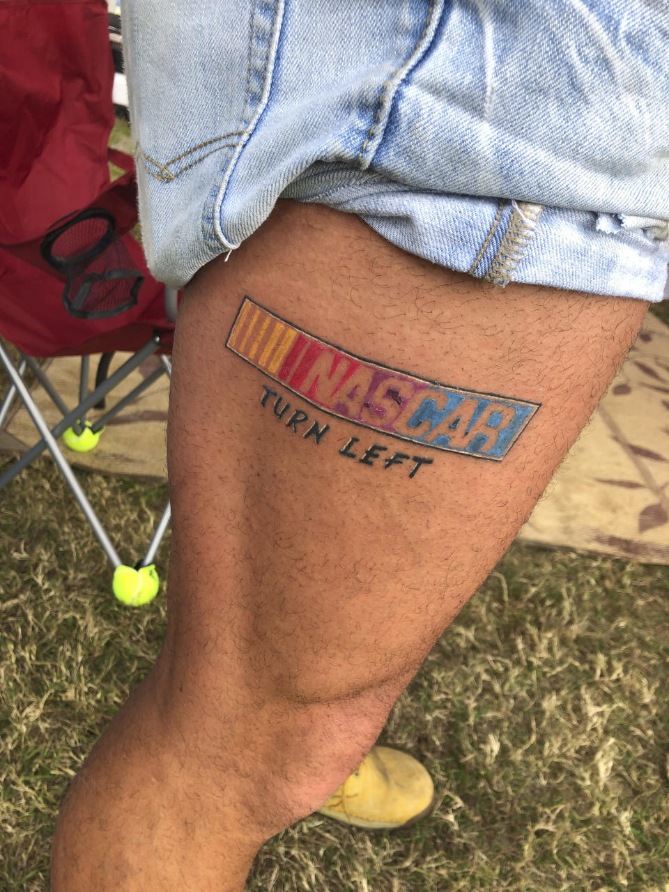 A race fan with a NASCAR tattoo is shown in the infield at the Daytona International Speedway before a truck race Friday, Feb. 12, 2021, in Daytona Beach, Fla. Daytona is used to shirtless fans partying in the infield. But what about maskless ones? Usually the biggest NASCAR party of the season, the sport will have to figure out how to police up to 30,000 fans who may have little interest in sticking to the pandemic guidelines. How many fans will actually come remains to be seen.(AP Photo/Daniel Gelston)