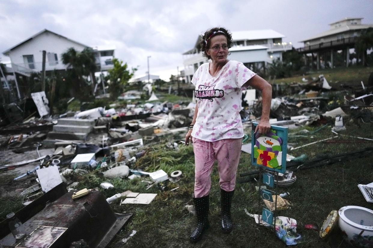 Wearing rain boots, Jewell Baggett stands in a grassy area with debris from destroyed mobile homes strewn around.