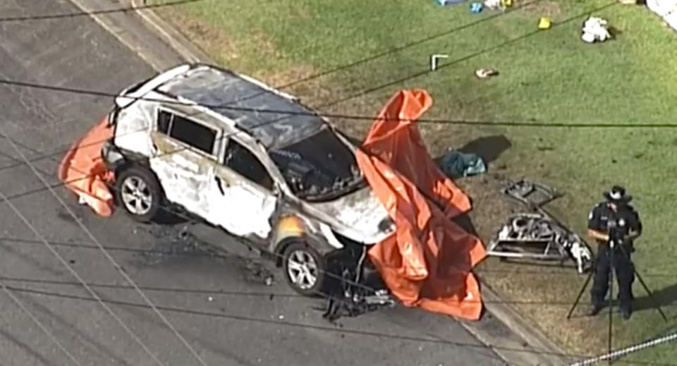 A burnt car sits destroyed on a Camp Hill street as police investigate it.