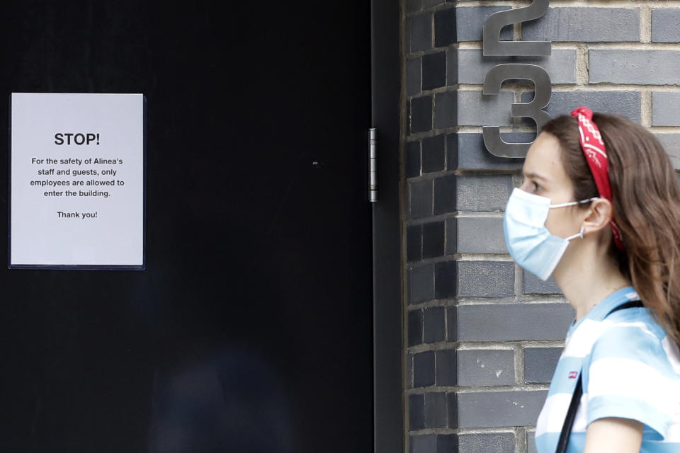 A woman walks near a sign posted at Alinea restaurant in Chicago, Saturday, June 20, 2020. Some of the world's best restaurants have had to make a quick pivot to weather the coronavirus. Alinea used to offer an 18-course tasting menu for $365; now it's making carryout meals for $49.94. (AP Photo/Nam Y. Huh)