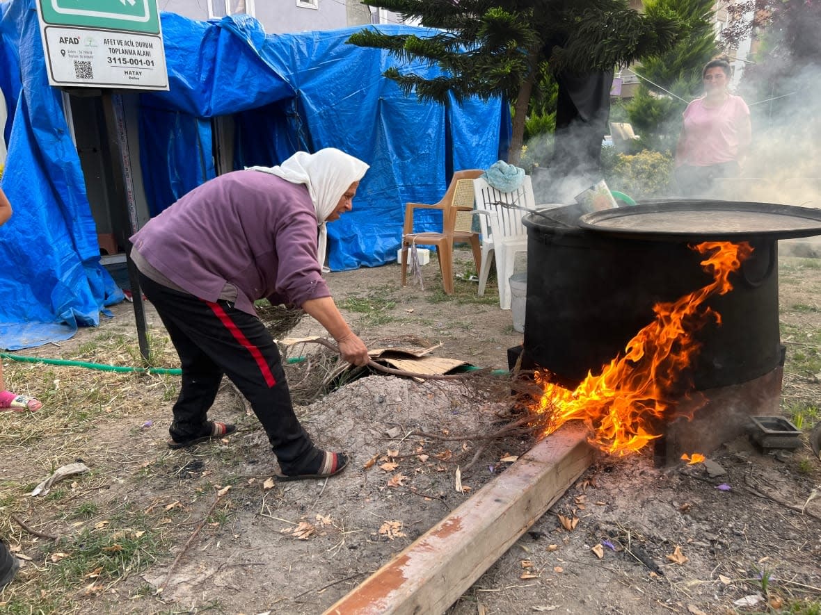 Emel Atici gathers dry branches to heat up water so people staying at the camp can have a weekly shower. Atici, 61, lost her son, daughter-in-law and grandson in the earthquakes in Antakya.  (Corinne Seminoff/CBC - image credit)