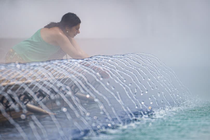 A woman cools off next to a public fountain in Bucharest, Romania, Wednesday, June 19, 2024.