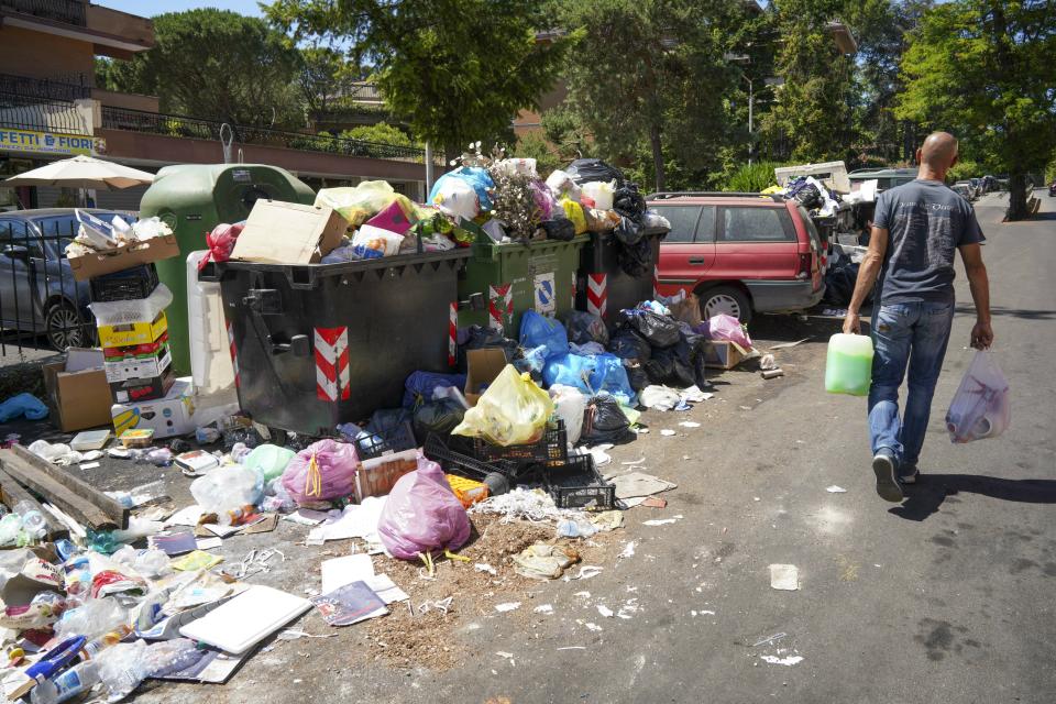 In this photo taken on Monday, June 24, 2019, a man walks past a pile of garbage in Rome. Doctors in Rome are warning of possible health hazards caused by overflowing trash bins in the city streets, as the Italian capital struggles with a renewed garbage emergency aggravated by the summer heat. (AP Photo/Andrew Medichini)