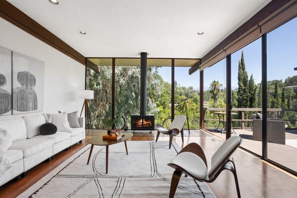 Floor-to-ceiling glazing wraps around the main living area, enhancing the intimate indoor-outdoor connection. The slender black freestanding fireplace radiates cozy, sleek vibes.