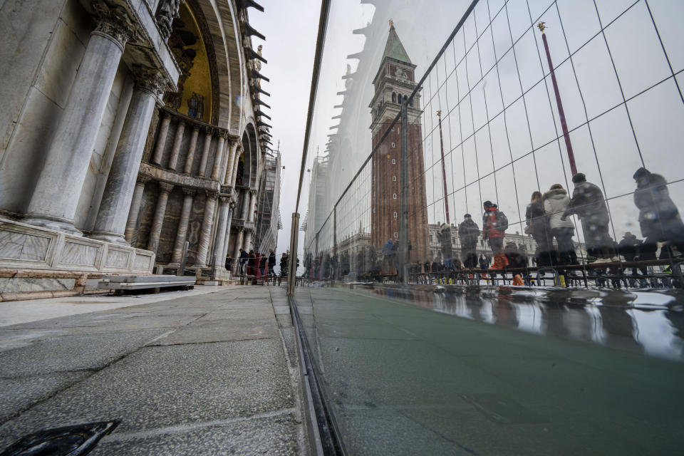 Tourists and residents walk on catwalks during a sea tide of around 97 centimeters (38.18 inches) to cross a flooded St. Mark's Square in Venice, northern Italy, Saturday, Dec. 10, 2022, where recently installed glass barriers prevent seawater from flooding the 900-year-old iconic St Mark's Basilica, left. St. Mark's Square is the lowest-laying city area and frequently ends up underwater during extreme weather. (AP Photo/Domenico Stinellis)