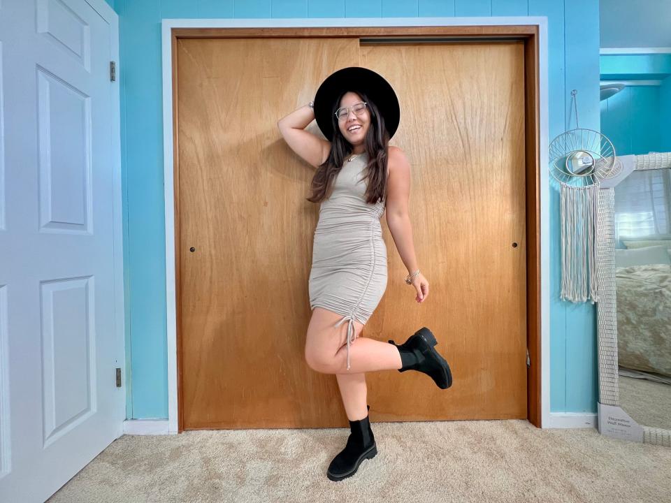 Author posing while wearing light grey dress, black booties, and a wide-brimmed black hat.