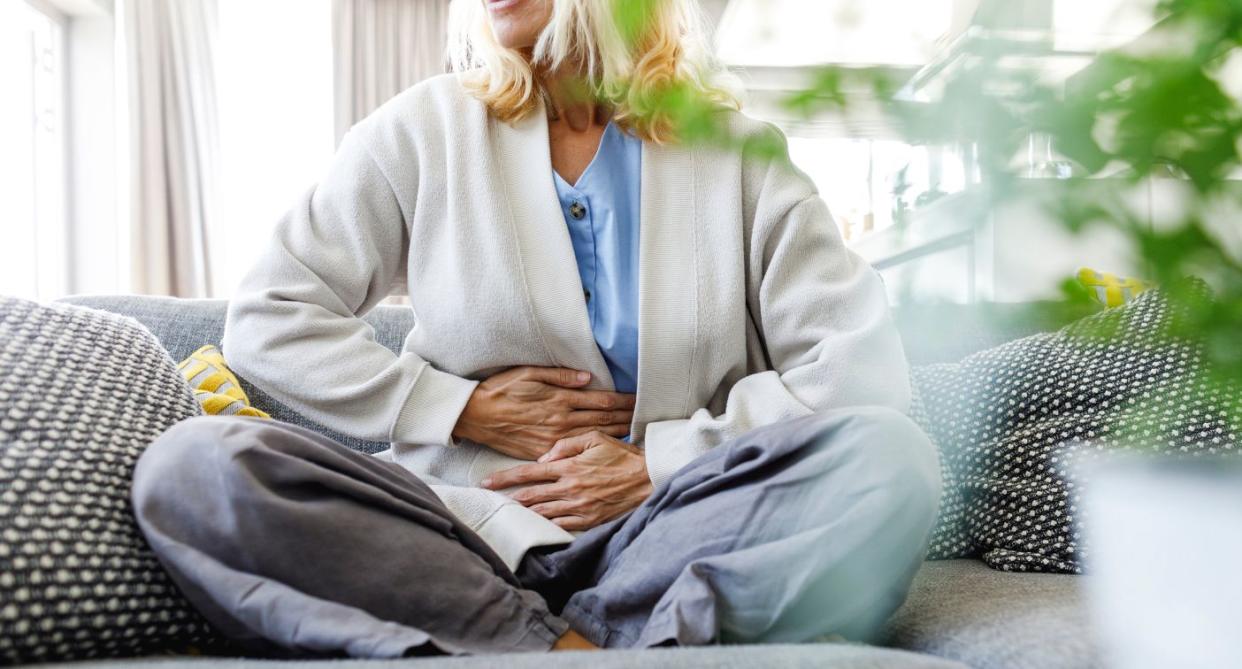 Woman sitting indoors in gut health pain holding stomach. (Getty Images)