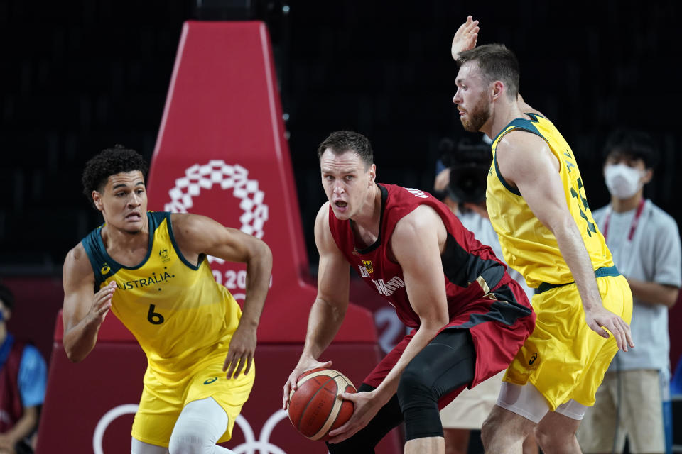 Germany's Johannes Voigtmann, center, passes between Australia's Josh Green, left, and Nic Kay, right, during a men's basketball preliminary round game at the 2020 Summer Olympics, Saturday, July 31, 2021, in Saitama, Japan. (AP Photo/Charlie Neibergall)