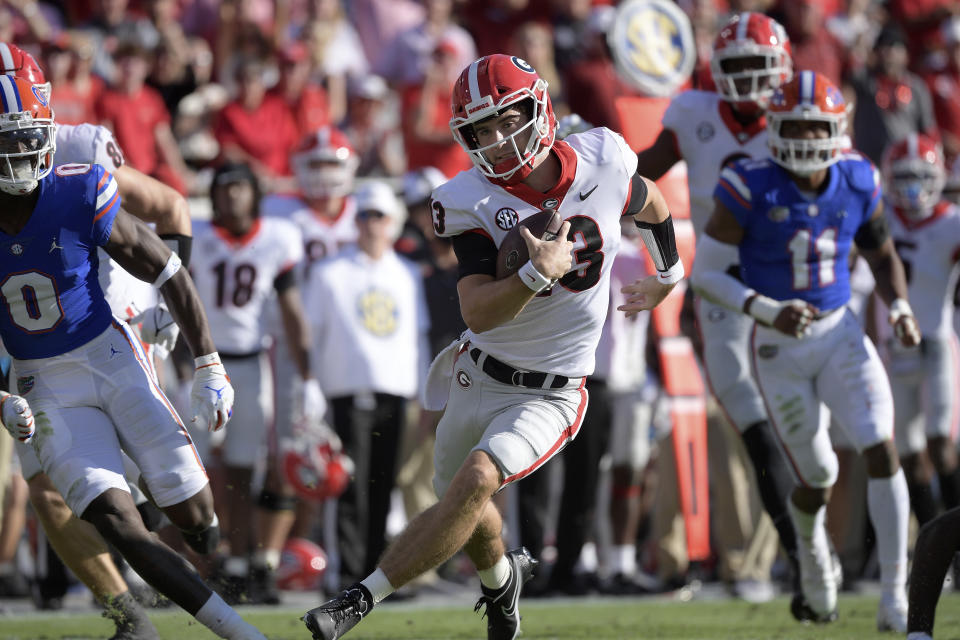Georgia quarterback Stetson Bennett (13) scrambles for yardage in front of Florida safety Trey Dean III (0) and linebacker Mohamoud Diabate (11) during the first half of an NCAA college football game, Saturday, Oct. 30, 2021, in Jacksonville, Fla. (AP Photo/Phelan M. Ebenhack)