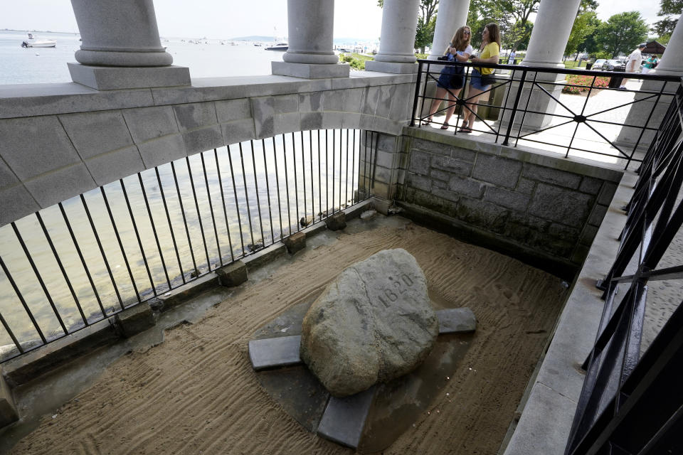 Visitors stand in a pavilion that shelters Plymouth Rock, below, in Plymouth, Mass., Wednesday, June 9, 2021. Archaeologists are excavating the grassy hilltop that overlooks iconic Plymouth Rock one last time before a historical park is built on the site. (AP Photo/Steven Senne)