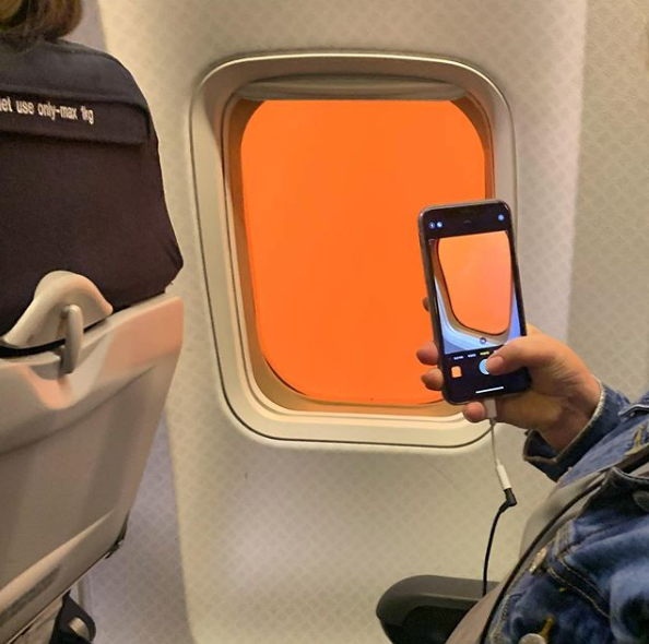 Pictured is a passenger taking a photo of a plane window with an orange sky. 