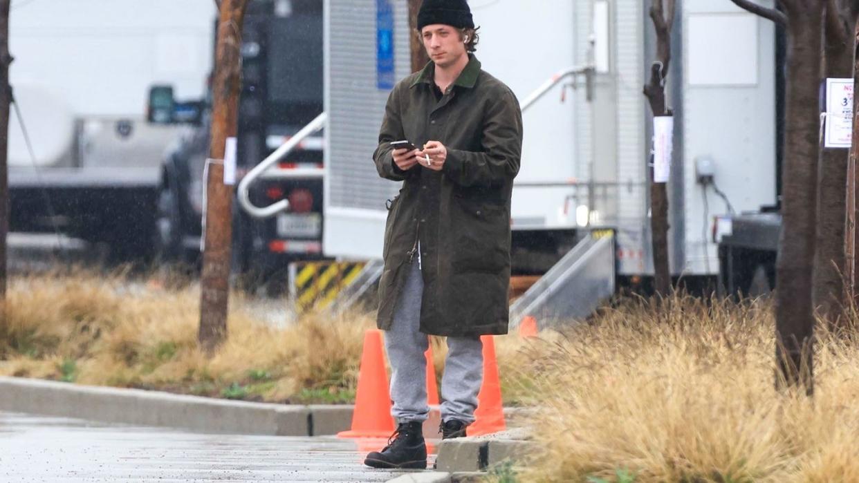 a person in a black coat and hat standing on a street corner