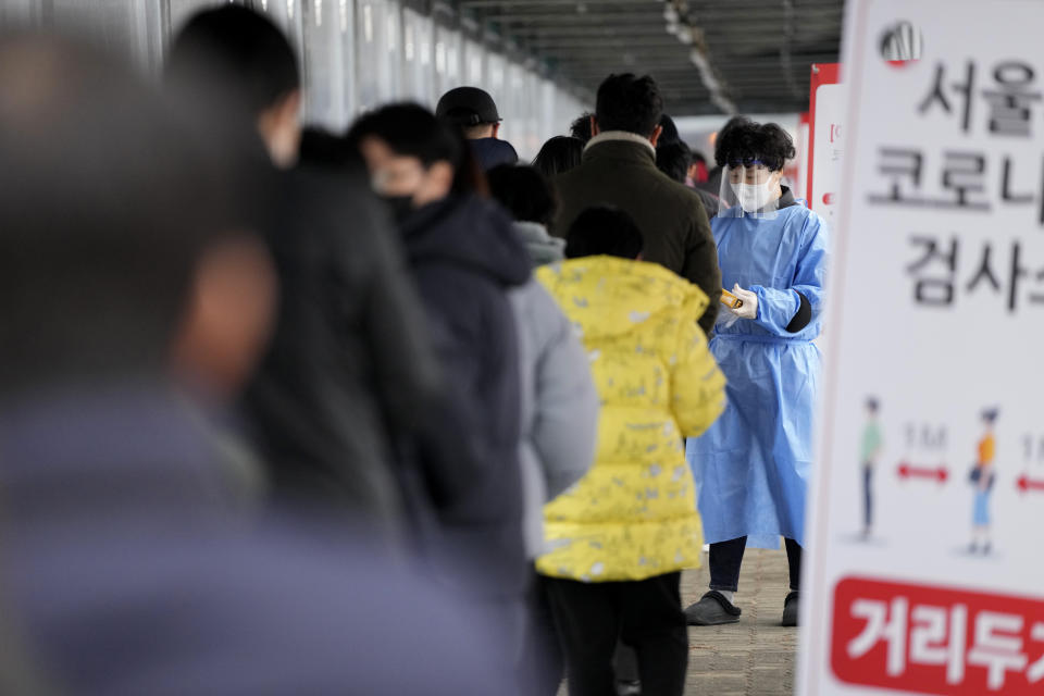 A health worker wearing protective gear holds plastic gloves for visitors at a temporary screening clinic for the coronavirus in Seoul, South Korea, Tuesday, Jan. 25, 2022. South Korea recorded more than 8,000 new coronavirus infections for the first time Tuesday as health authorities reshape the country's pandemic response to address a surge driven by the highly contagious omicron variant. (AP Photo/Lee Jin-man)