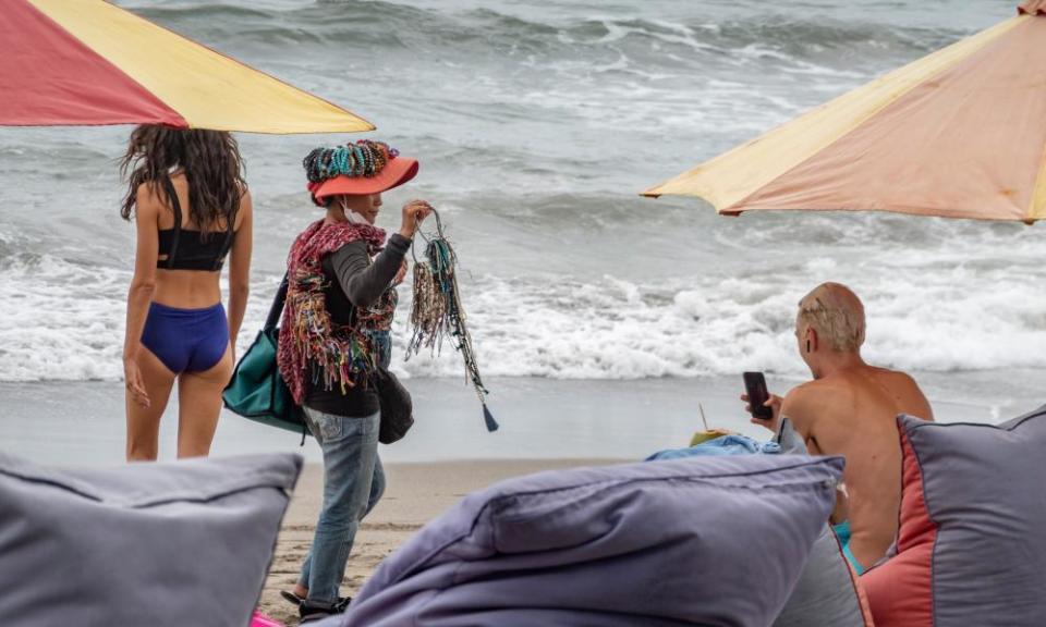 A souvenirs vendor walks among tourist at a beach in Canggu.