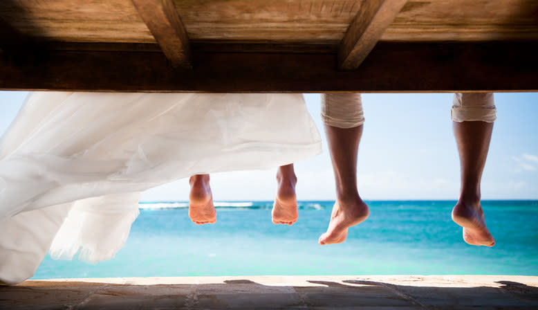 A barefoot bride and a man sitting by the ocean