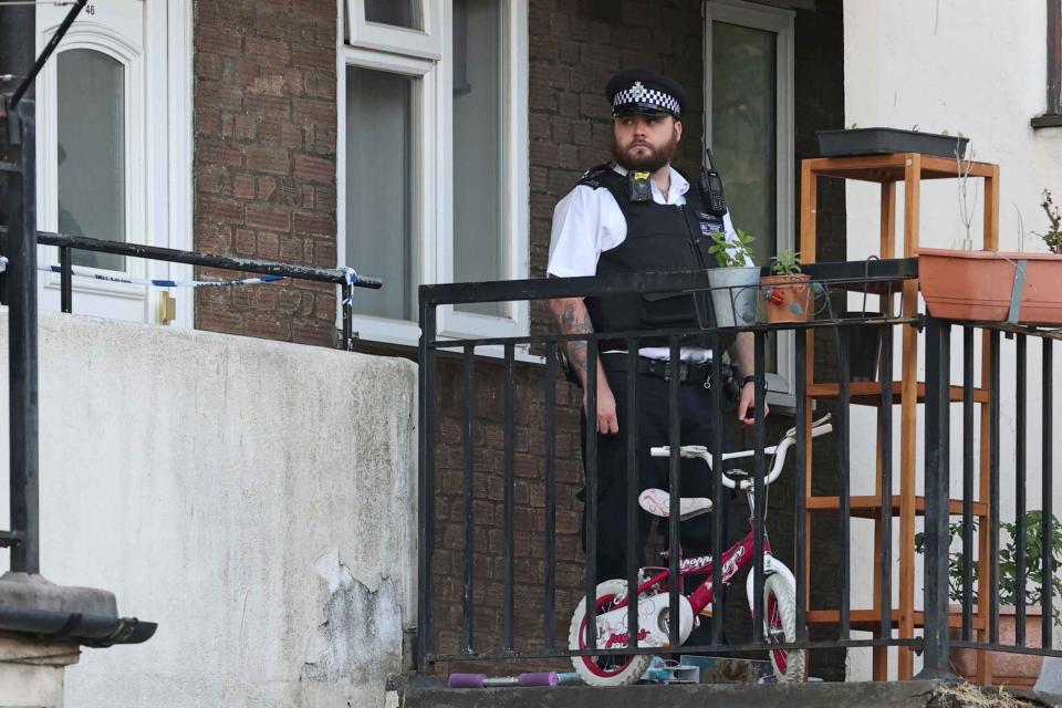 Horror: a police officer stands guard outside the flat in Mitcham today (Evening Standard / eyevine)