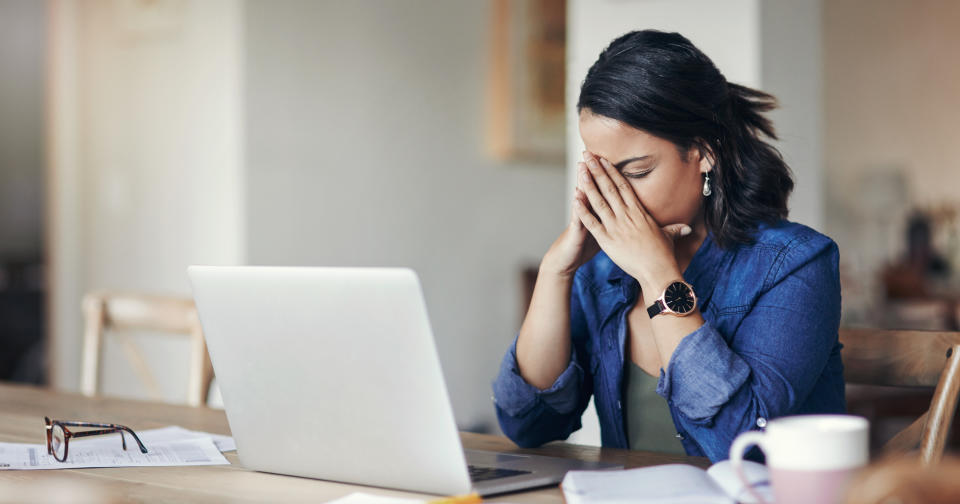 A woman looking stressed while using a laptop at home.