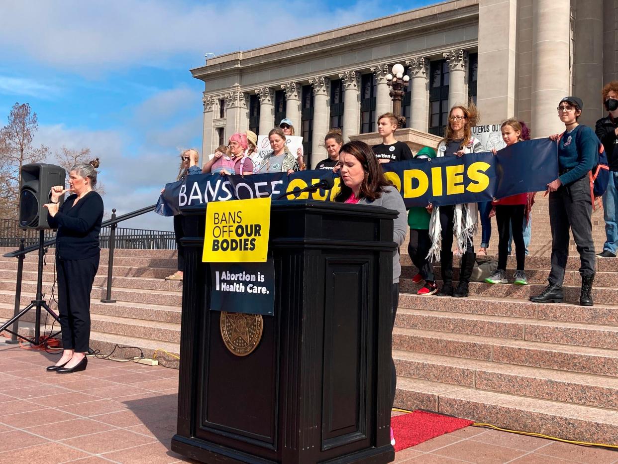 A woman speaks at a podium in front of a capitol building behind a banner that reads "Bans off our bodies."