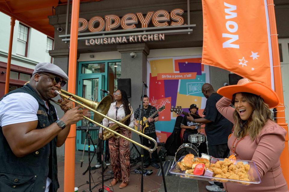 Sammie 'Big Sam' Williams of Big Sam’s Funky Nation, left, performs next to social media influencer Jennifer Palpallatoc Perrault, a fashion and lifestyle blogger, at the re-opening of the Popeyes Louisiana Kitchen location on Canal Street in the French Quarter in New Orleans, Monday, March 28, 2022. The New Orleans restaurant is the first-ever Popeyes in the United States to feature modernized design including self-order kiosks, order ready boards, and dedicated areas for digital order pickup. Photo by Matthew Hinton