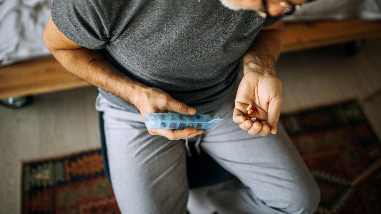 senior man taking medications from a daily pill organizer