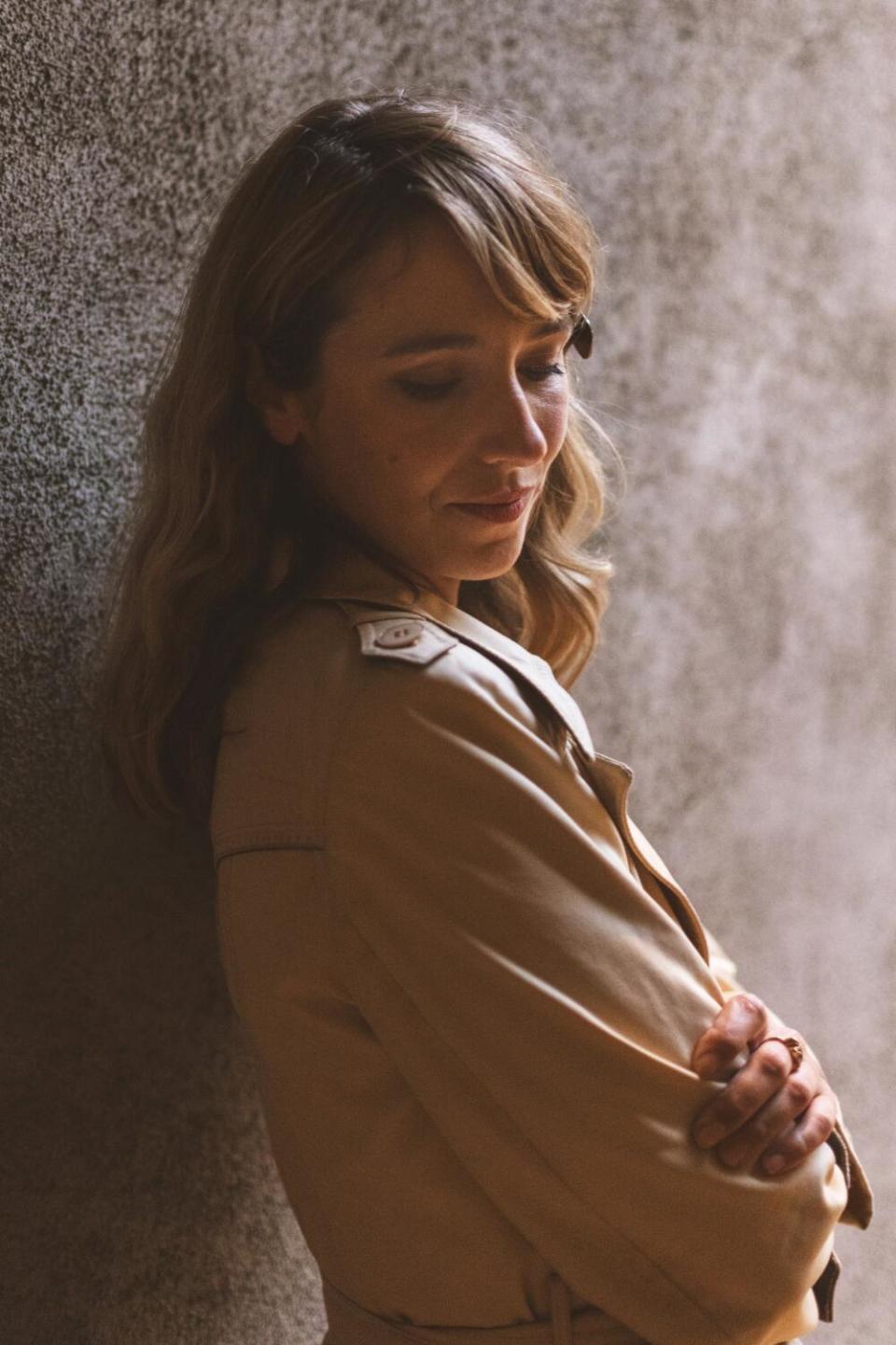 Molly Lewis leans against a wall, arms crossed, and peers into the camera.