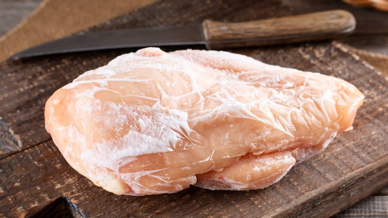 Close-up of a frozen chicken breast and knife on a cutting board