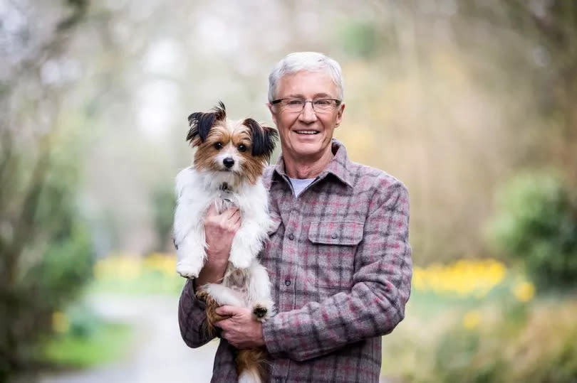 Paul O'Grady holding a dog in  the countryside