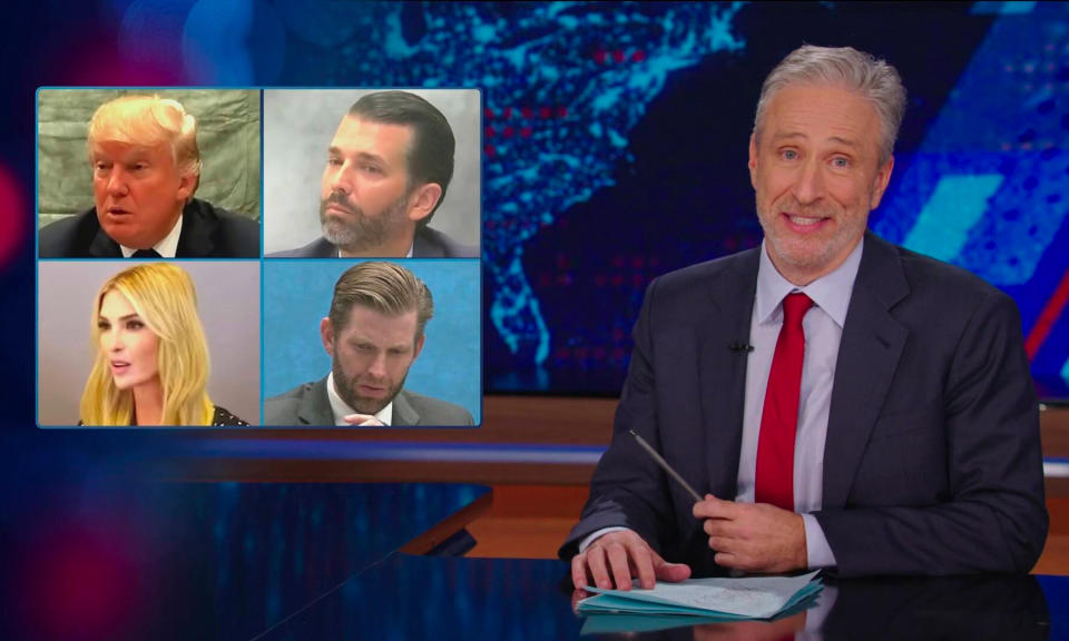Still of Jon Stewart’s 2024 return to The Daily Show. The host sits at a desk with an overlay showing pictures of Donald Trump and his children.
